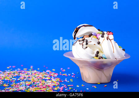 Frozen yogurt con cioccolato e caramelle cioccolato topping su sfondo blu con spruzzi di Rainbow Foto Stock