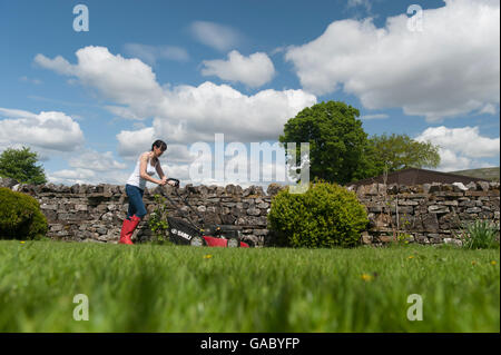 Signora la falciatura giardino prato con alimentata a benzina tosaerba. Hawes, North Yorkshire, Regno Unito. Foto Stock