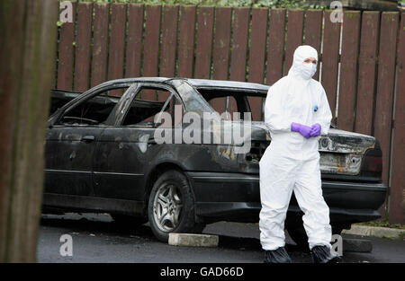 Un ufficiale forense della polizia esamina un'auto bruciata, nella tenuta di Creggan a Derry, che si ritiene sia stata usata da un pistolero in cui un ufficiale di polizia è stato oggi blasted con un fucile fuori di una scuola nell'Irlanda del Nord. L'ufficiale è stato ambushed a Bishop St, vicino al centro di Londonderry quando ha tirato in su nella sua automobile mentre centinaia degli allievi sono arrivati per le classi. Foto Stock