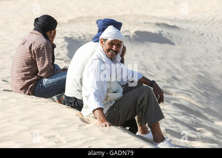 I beduini in appoggio sulla sabbia durante la gita turistica sui cammelli intorno all'inizio del deserto del Sahara a Douz, Kebili, Tunisia. Foto Stock