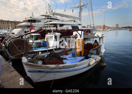 I pescatori tendono le loro reti nel Vecchio Porto della città mediterranea francese di Marsiglia. Partiscono prima dell'alba, tornando a metà mattina per ormeggiare le loro piccole barche da pesca tra i megayachts dei superricchi. Foto Stock