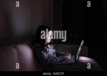 Bambina, seduta in una buia, giocando con il computer portatile Foto Stock