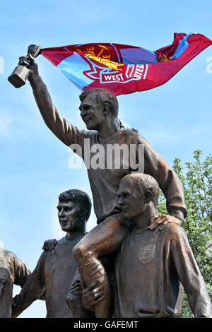 Parte della Coppa del mondo di football giocatori scultura con Bobby Moore con la World Cup Trofeo più tifosi West Ham banner fisso alla tazza in Upton Park Foto Stock