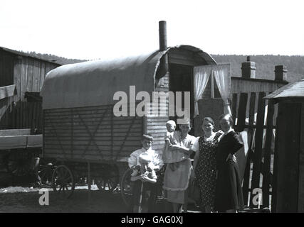 1930s, storico madre con bambino e i figli piccoli stand al di fuori della loro casa. un caravan di legno su ruote, su un maso vicino Elbogen, Sudentenland, in pre-ww11 Cecoslovacchia. Foto Stock