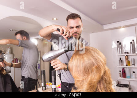 L'uomo parrucchiere colpo di asciugatura rullo a pettine capelli donna, vista laterale Foto Stock