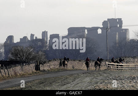 Le rovine del castello di Middleham si ergono sopra la nebbia mentre le corde di cavalli da corsa si fanno strada sulle galoppe sopra Middleham, North Yorkshire. Foto Stock