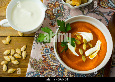 Zucca piccante squash minestra in crema con la panna e i semi di zucca nella ciotola bianco, la crema di latte in un creamer e crostini in un serving dis Foto Stock