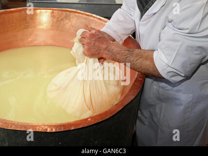 Pastore casaro raccoglie il formaggio dal grande paiolo di rame con il latte di vacca e latte di capra Foto Stock