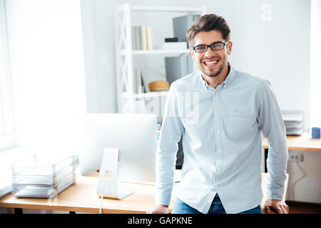 Ritratto di giovane sorridente imprenditore in bicchieri in piedi in ufficio Foto Stock
