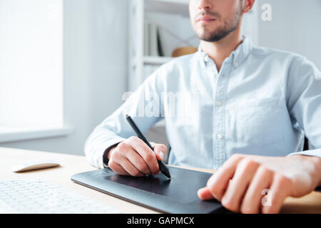 Primo piano nero della tavoletta grafica utilizzata da giovane serio designer in ufficio Foto Stock