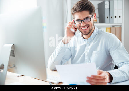 Sorridenti imprenditore azienda documenti e parlando al telefono cellulare in ufficio Foto Stock