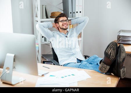 Allegro giovane impreditore seduti a tavola con laptop e stretching in ufficio Foto Stock