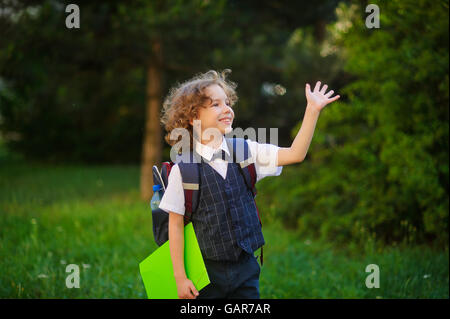 Curly blonde prima-grader va a scuola. La scuola primaria gli studenti ben vestiti. Dietro il bambino della scuola zaino. Il sch Foto Stock