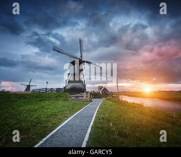 Paesaggio con tradizionali mulini a vento olandese e il percorso nei pressi di canali d'acqua. Nuvole al tramonto colorato in primavera. Kinderdijk Foto Stock