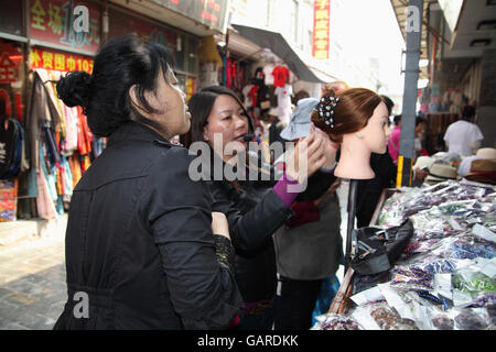 Una donna di pettini e mette insieme una parrucca su un manichino a galanterie, parla al microfono e mostra un potenziale cliente fasce per capelli e le graffe. Foto Stock