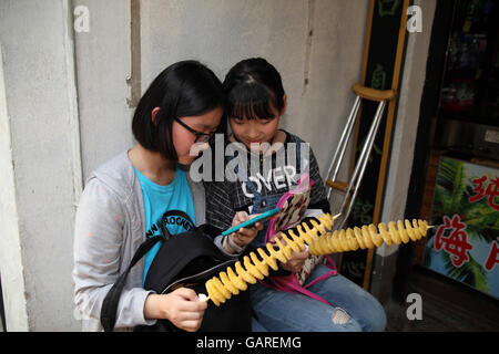 Due ragazze cinesi siedono insieme con la caramella nelle loro mani, essi sono la visione di un video su uno smartphone appartenente ad uno di essi. Tongli , Cina. Foto Stock