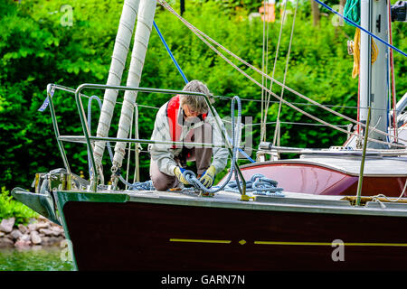 Motala, Svezia - 21 Giugno 2016: Senior donna legatura di un nodo sulla prua di una barca a vela di colore marrone. La vita reale situazione. Foto Stock