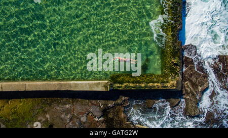 Un nuotatore solitario nuota giri nell'oceano Austinmer rock pools, visto dall'alto. Foto Stock