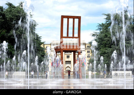 Fontane d'acqua davanti a 'la sedia rotta' una statua eretta per promuovere la Campagna Internazionale per mettere al bando le mine terrestri a Place des Nations. Sullo sfondo si trovano i quartier generali europei delle Nazioni Unite. Foto Stock