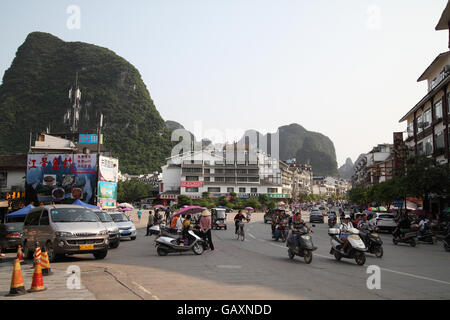 Auto, motocicli e biciclette visto su una strada in background sono la zona di Guilin colline carsiche e i cartelloni in cinese. Yangshuo, Guangxi, Cina. Foto Stock
