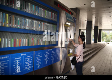 Una giovane donna Chine utilizzando un sistema automatico di self service library macchina da affittare o prendere in prestito un libro. Shenzhen, Cina Foto Stock