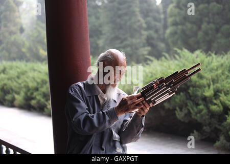 Un vecchio uomo cinese con la barba bianca esamina la sua Sheng Yu o che è una bocca cinese soffiata free reed di strumento a fiato Foto Stock