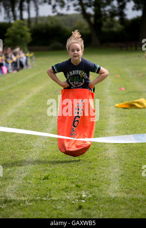 Ragazza a metà in aria competere nel sacco gara st James scuola primaria la giornata dello sport Chipping Campden Regno Unito Foto Stock