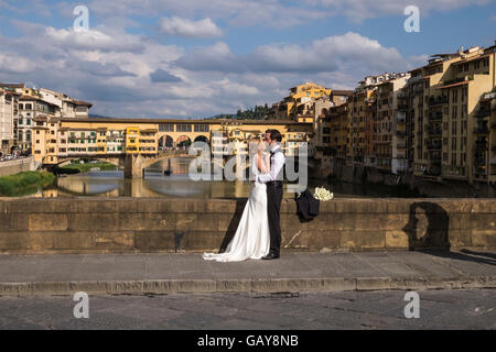 Coppie in viaggio di nozze haveing loro le foto scattate sul Ponte Santa Trinita con il Ponte Vecchio in background, Firenze, Toscana Foto Stock
