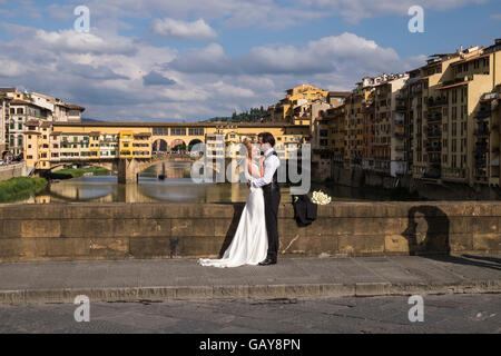 Coppie in viaggio di nozze haveing loro le foto scattate sul Ponte Santa Trinita con il Ponte Vecchio in background, Firenze, Toscana Foto Stock