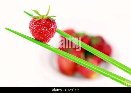 Fragola rossa di attesa con bacchette verde in primo piano sullo sfondo bianco Foto Stock