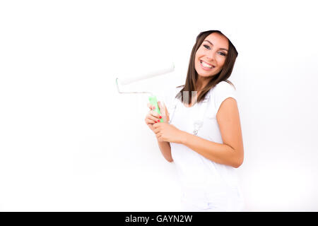 Una giovane e bella donna adulta pittura un muro nella sua abitazione in bianco. Foto Stock