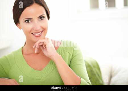 Sorridente donna caucasici in camicia verde guardando la telecamera mentre a mettere mano sul mento in interni - Spazio di copia Foto Stock