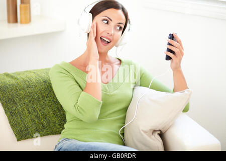Vita ritratto di una giovane donna godendo la musica sulle cuffie mentre è seduto in ambienti interni Foto Stock
