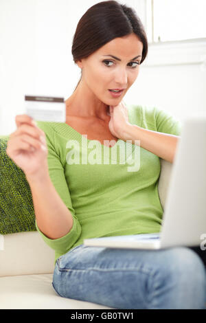 Giovane donna guardando sorpresi della carta di credito mentre si effettua un pagamento elettronico sul suo computer portatile Foto Stock