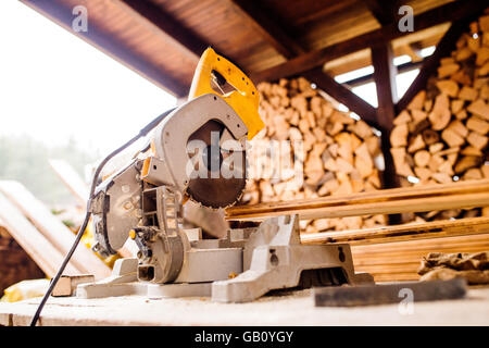 Sega circolare prevista sul tavolo, la pila di legno dietro di essa Foto Stock