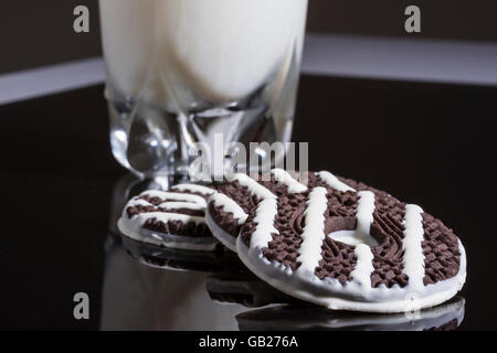 Biscotti al cioccolato bianco con strisce color crema e un bicchiere di latte in un buio e la superficie riflettente. Foto Stock