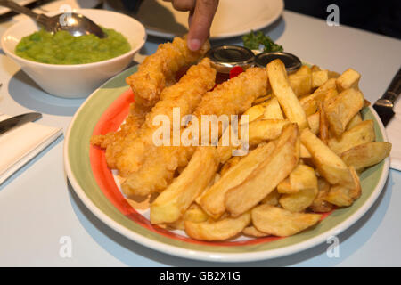 Un diner preleva un chip al Poppies pesce e Chip shop a Londra, Inghilterra. Foto Stock