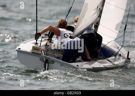 Le 470 donne della Gran Bretagna Saskia Clark e Christina Bassadone anatra sotto il boom, mentre si ribattano durante l'odierna gara di medaglie al Centro di vela dei Giochi Olimpici di Pechino 2008 a Qingdao, Cina. Foto Stock