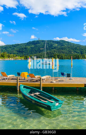 WORTHERSEE LAGO, Austria - giu 20, 2015: imbarcazioni turistiche e sdraie con ombrelloni sul molo in legno del bellissimo lago alpino di mosto di malto Foto Stock