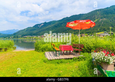 Lago Weissensee, Austria - Lug 6, 2015: ombrelloni con lettini per prendere il sole sulla spiaggia al lago Weissensee in estate il paesaggio di montagna delle Alpi Foto Stock