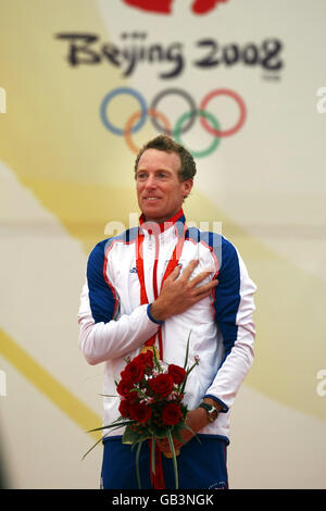 Paul Goodison della Gran Bretagna guarda l'Union Jack che viene sollevato dopo aver vinto una medaglia d'oro nella classe laser maschile al Centro di vela dei Giochi Olimpici di Pechino 2008 a Qingdao, Cina. Foto Stock