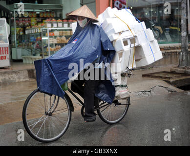 Un ciclista durante una doccia a pioggia a ho Chi Minh City, Vietnam. Foto Stock