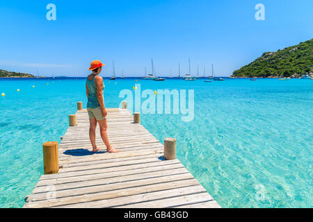 Giovane donna turista in piedi sul pontile in legno sulla spiaggia di Santa Giulia guardando il mare azzurro, Corsica, Francia Foto Stock