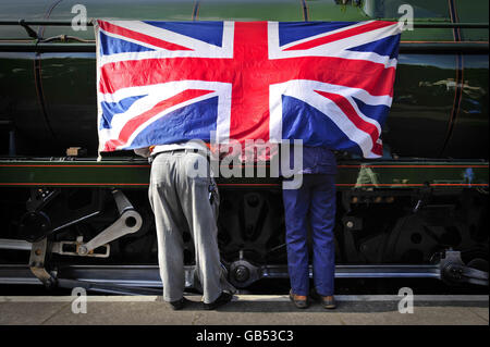 Due zampe di uomini escono da sotto una bandiera dell'Unione, al lancio dell'ultima locomotiva Southern Railway West Country Class No. 34046 chiamata Braunton alla stazione di Lydeard vicino a Taunton, Somerset dopo un esteso progetto di ristrutturazione. Foto Stock