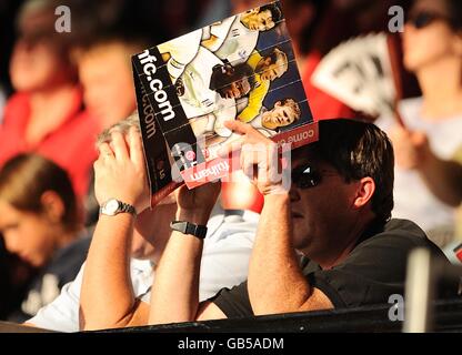 Un tifoso di calcio scudi gli occhi dal sole con un programma di giornate di partite nei paletti. Foto Stock