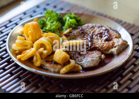 Le braciole di maiale alla griglia con Patatine fritte ricci e broccoli cotti al vapore Foto Stock