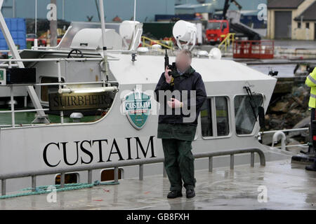 I REDATTORI SI PREGANO DI NOTARE I VOLTI OSCURATI DALL'ASSOCIAZIONE STAMPA SU RICHIESTA DELLA POLIZIA. Arbed Gardai sicuro Castletown Bere Pier in Co. Cork in attesa dell'arrivo dello yacht di lusso 'Dances with Waves' che è stato sequestrato al largo della costa occidentale dell'Irlanda, ieri portando un enorme raggio di cocaina. Foto Stock