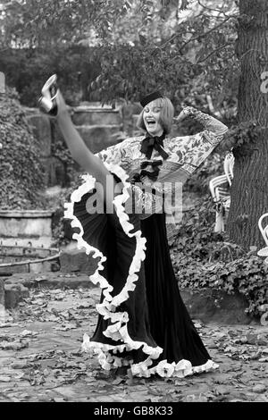 Nell Campbell rivestito in una creazione da Zandra Rhodes, mostrato nel giardino del Les Ambassadeurs Club. Nell indossa una blusa in chiffon a tutta lunghezza multicolore con una gonna nera a pieghe in raso e un cappello da pillola. Foto Stock