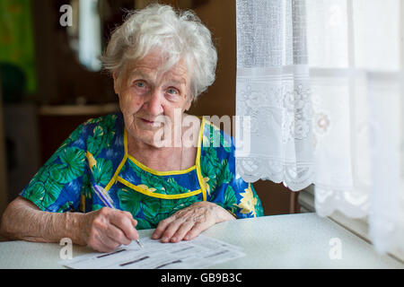 Una donna anziana riempie le forme utilities seduta a tavola in casa. Foto Stock