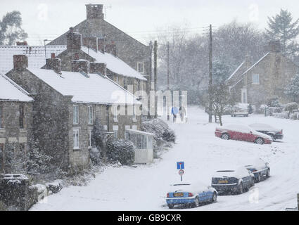 La gente cammina un cane mentre la neve cade nel villaggio di Lockton ai margini del North Yorkshire Moors National Park, mentre un fronte meteorologico artico colpisce il Regno Unito. Foto Stock